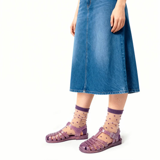 Person wearing purple sandals and socks with a blue denim skirt on a white background
