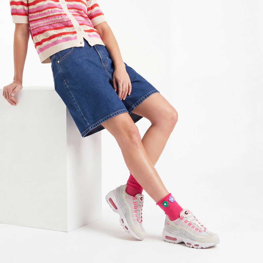Person wearing a striped sweater, denim shorts, and pink sneakers on a white background