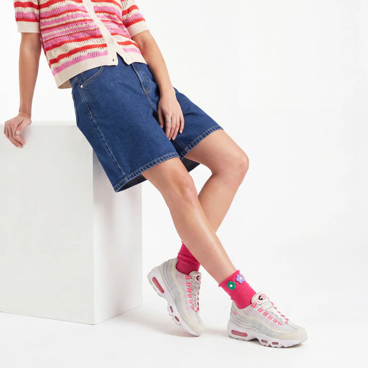 Person wearing a striped sweater, denim shorts, and pink sneakers on a white background
