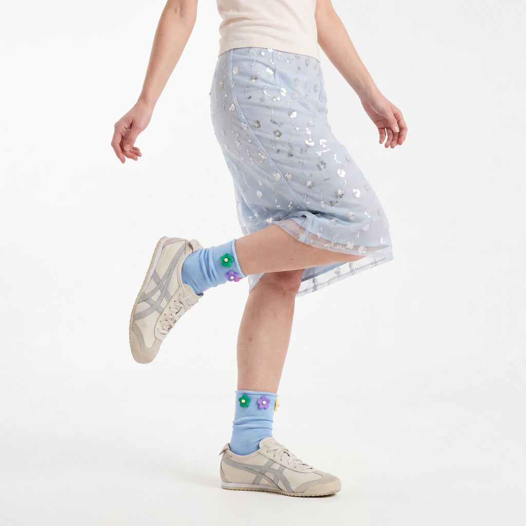 Person wearing a light blue skirt with star patterns and light blue socks with flower designs on a white background.