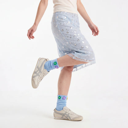 Person wearing a light blue skirt with star patterns and light blue socks with flower designs on a white background.