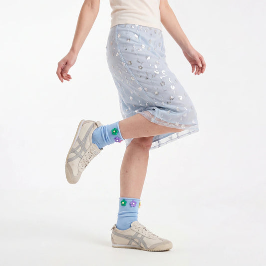Person wearing a light blue skirt with star patterns and light blue socks with flower designs on a white background.
