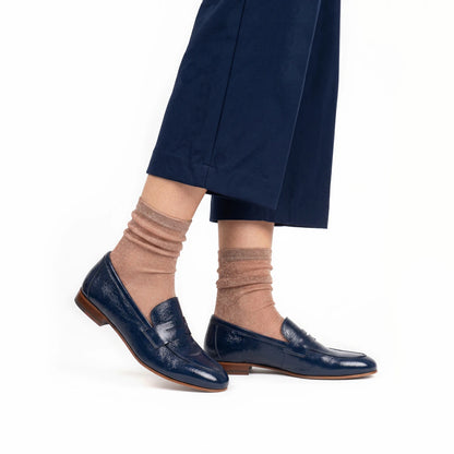 Navy blue loafers worn with rose gold socks and navy pants on a white background