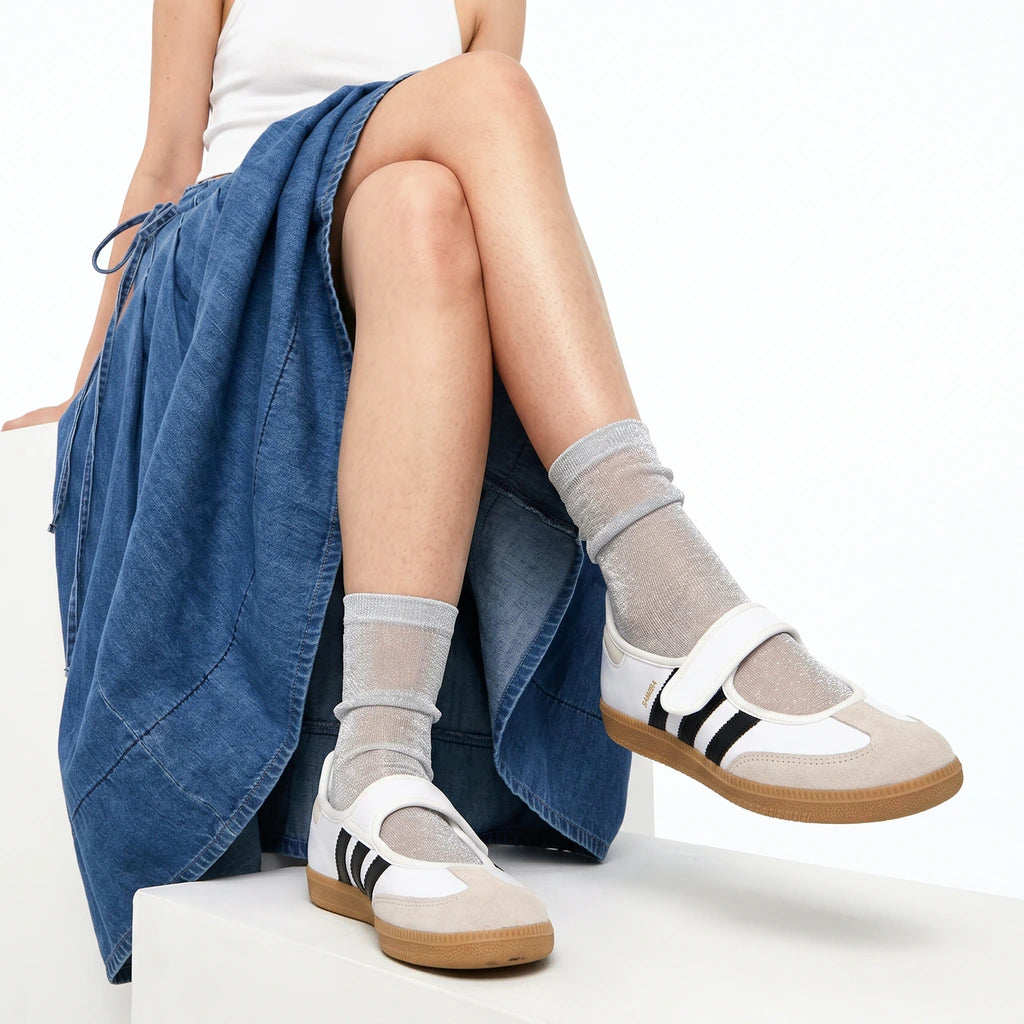 Person wearing white sneakers with brown soles and silver socks, sitting on a white surface with a blue garment.