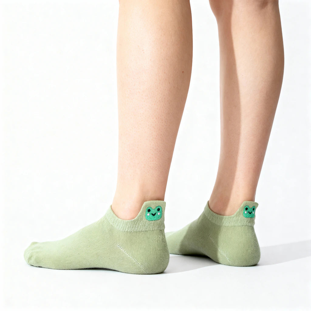 Green socks with smiley frog face design worn by a person on a white background