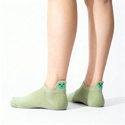 Green socks with smiley frog face design worn by a person on a white background