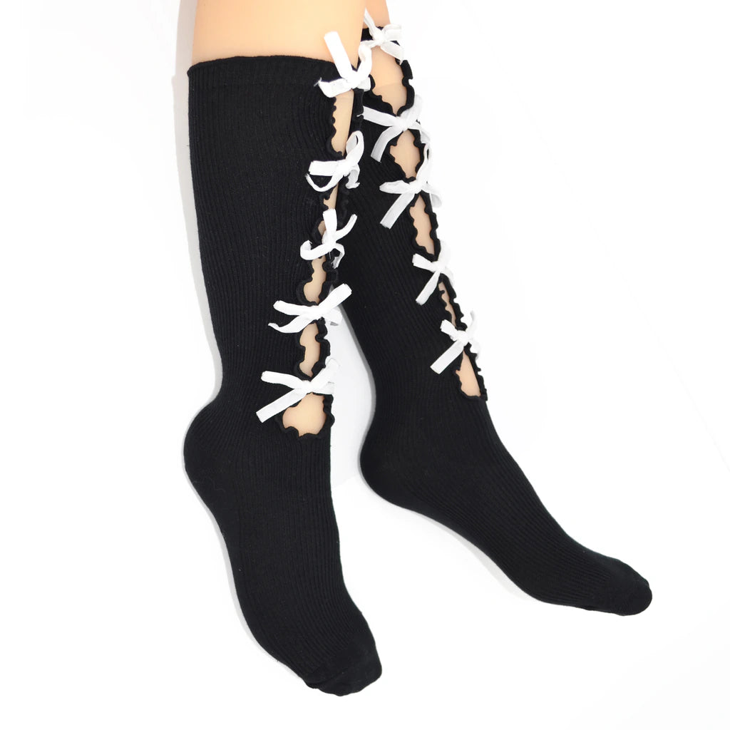 A pair of black knee-high socks with white lace-up detailing running up the front, shown worn on a person's legs against a plain white background.