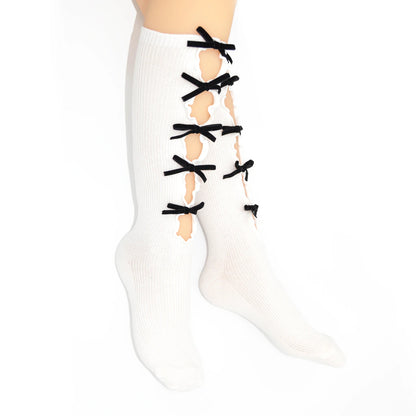 White knee-high ribbed socks with black ribbon laces tied across the front and distressed cutouts showing skin, modeled on a leg against a white background.