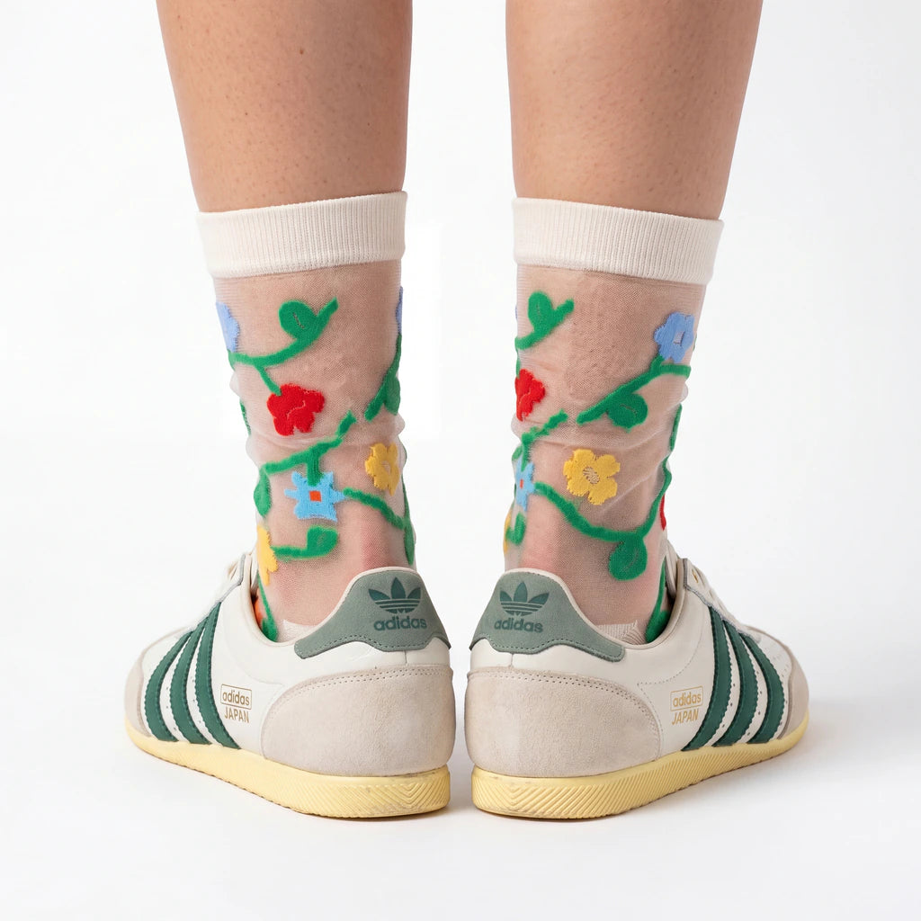 Transparent socks with floral designs worn with Adidas shoes on a white background