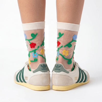 Transparent socks with floral designs worn with Adidas shoes on a white background