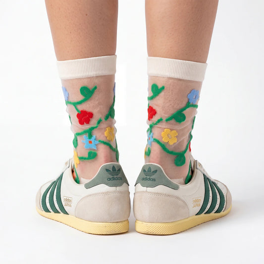 Transparent socks with floral designs worn with Adidas shoes on a white background