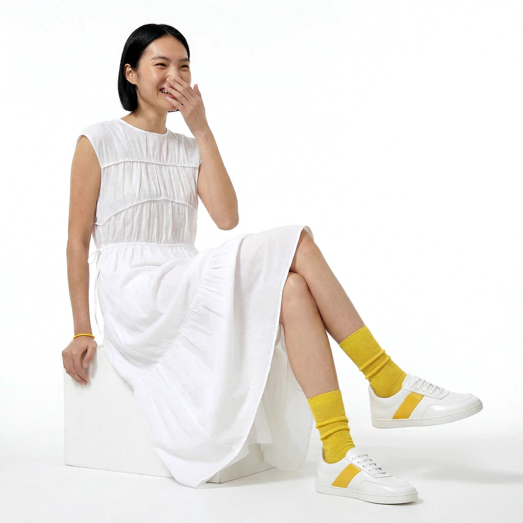 Woman wearing a white dress and yellow socks sitting on a white background