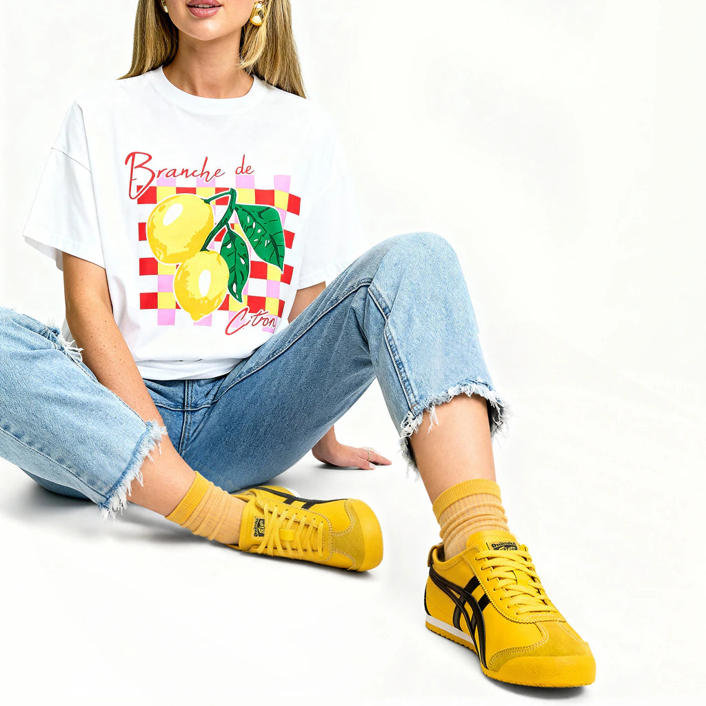 Person wearing a white t-shirt with a lemon design, blue jeans, and yellow sneakers on a white background
