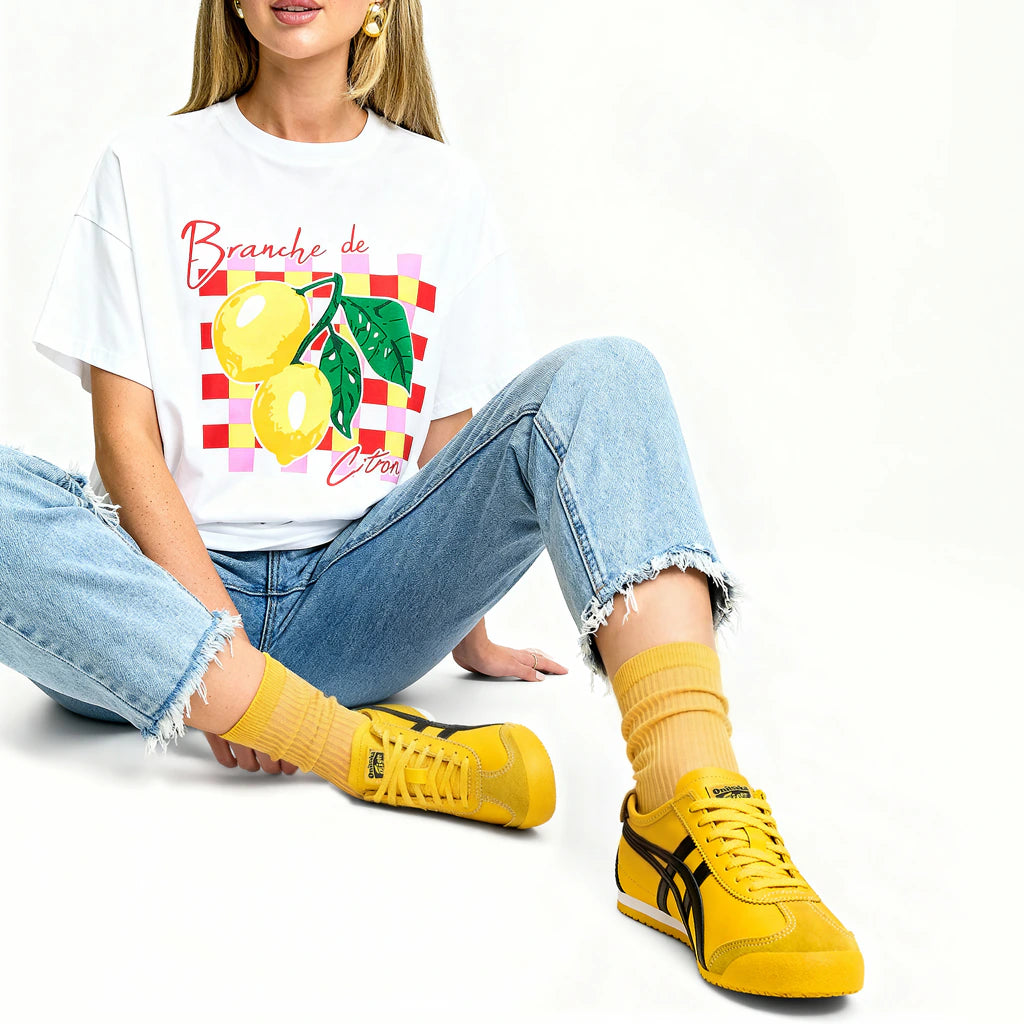 Person wearing a white t-shirt with a lemon design, blue jeans, and yellow sneakers on a white background
