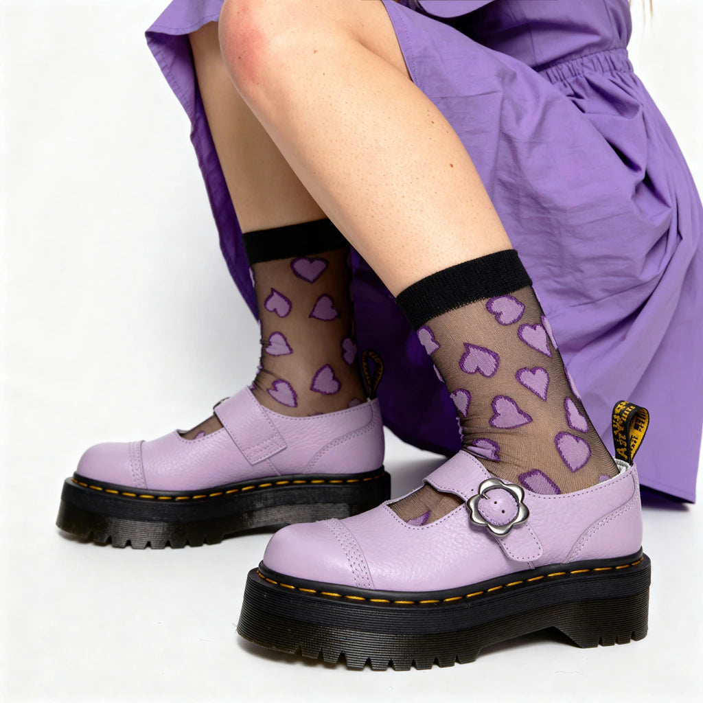 Person wearing purple shoes with black soles and a skirt, sitting on a white background.