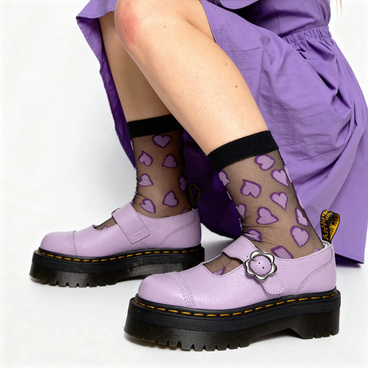 Person wearing purple shoes with black soles and a skirt, sitting on a white background.