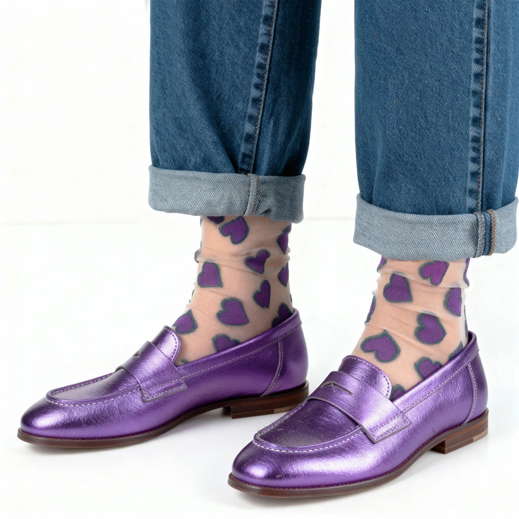 Purple loafers worn with blue jeans and purple heart-patterned socks on a white background