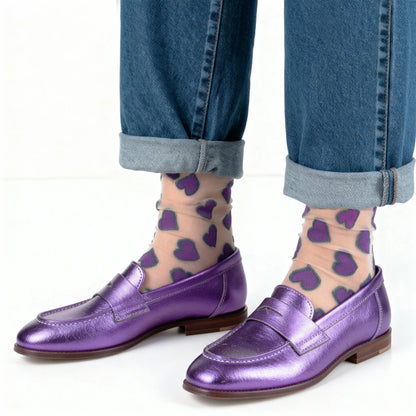 Purple loafers worn with blue jeans and purple heart-patterned socks on a white background