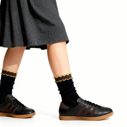 Person wearing black socks with brown trim and Adidas shoes on a white background
