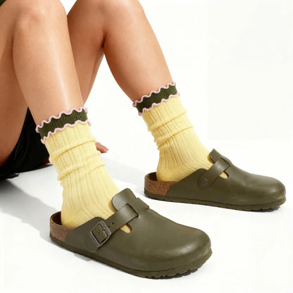 Person wearing yellow socks with green trim and green clogs on a white background