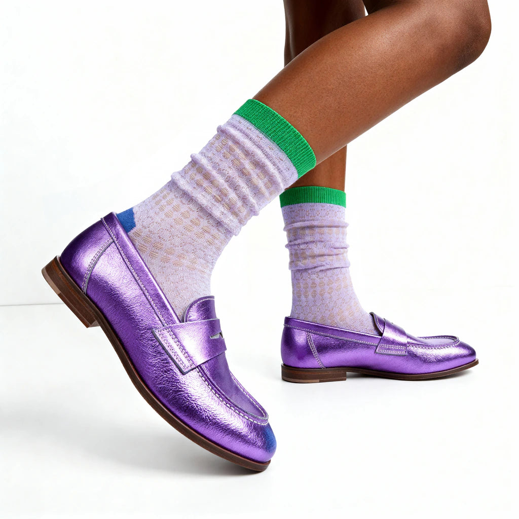 Purple loafers worn with lilac socks featuring green trim on a white background