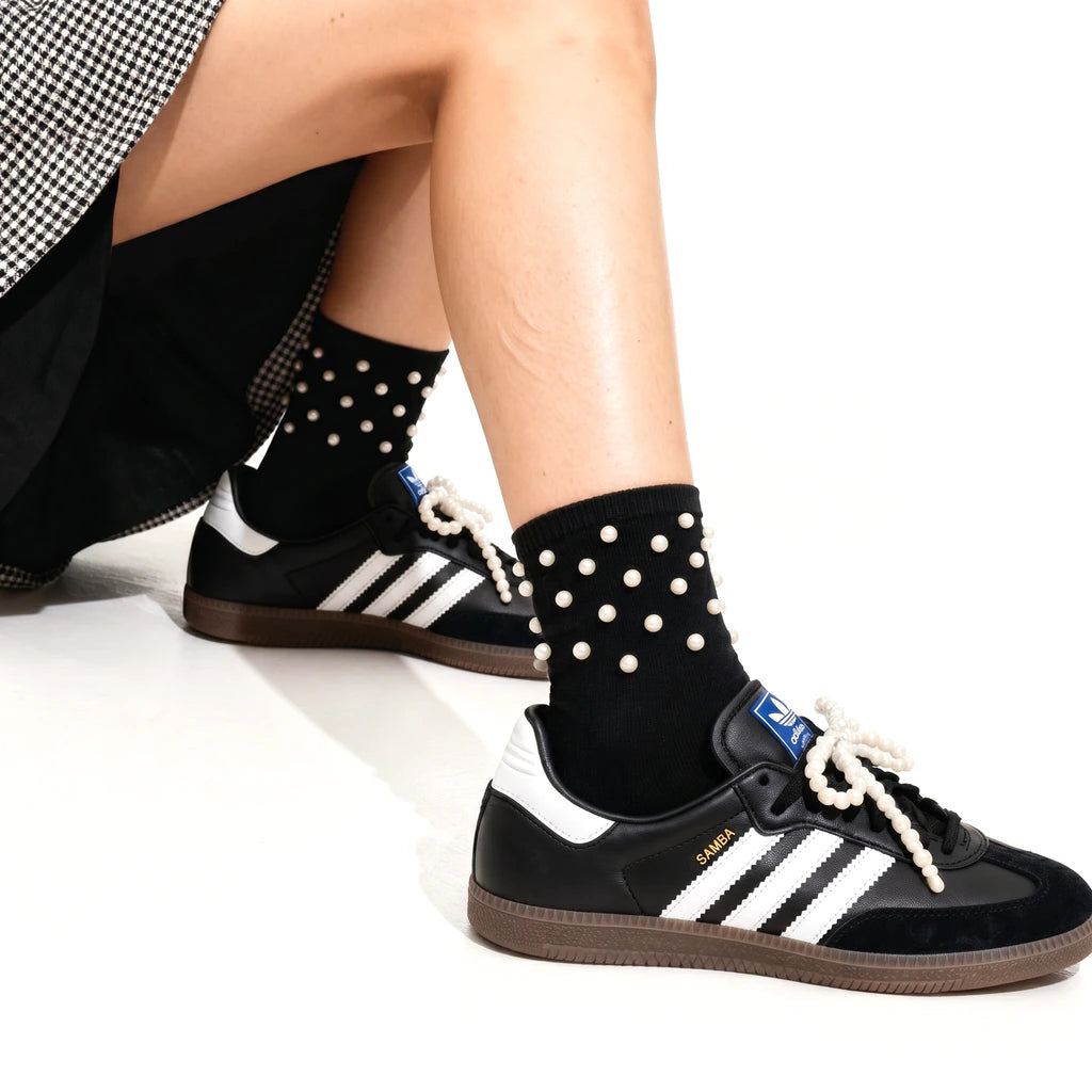 Person wearing black Adidas sneakers with white polka dot socks on a white background