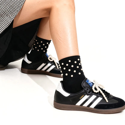 Person wearing black Adidas sneakers with white polka dot socks on a white background