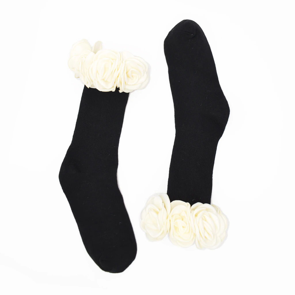 A pair of black crew socks with large white fabric flower embellishments at the top and bottom cuffs, displayed on a plain white background.