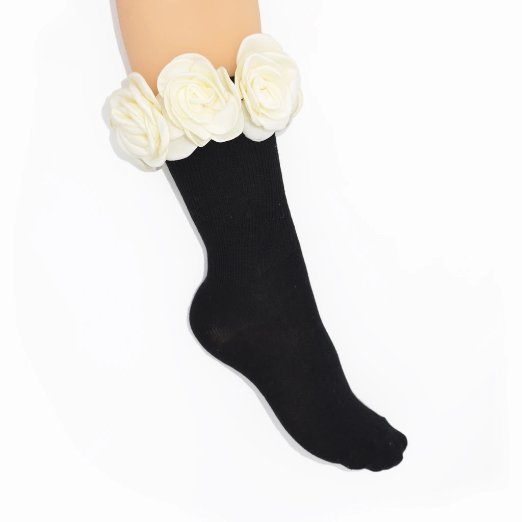 A black ankle sock worn on a leg, decorated with three large white fabric roses at the top, shown against a plain white background.