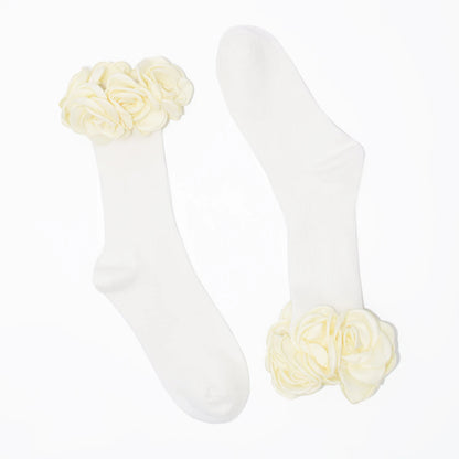 A pair of white crew socks with large cream-colored fabric roses at the top cuff, displayed on a clean white background.