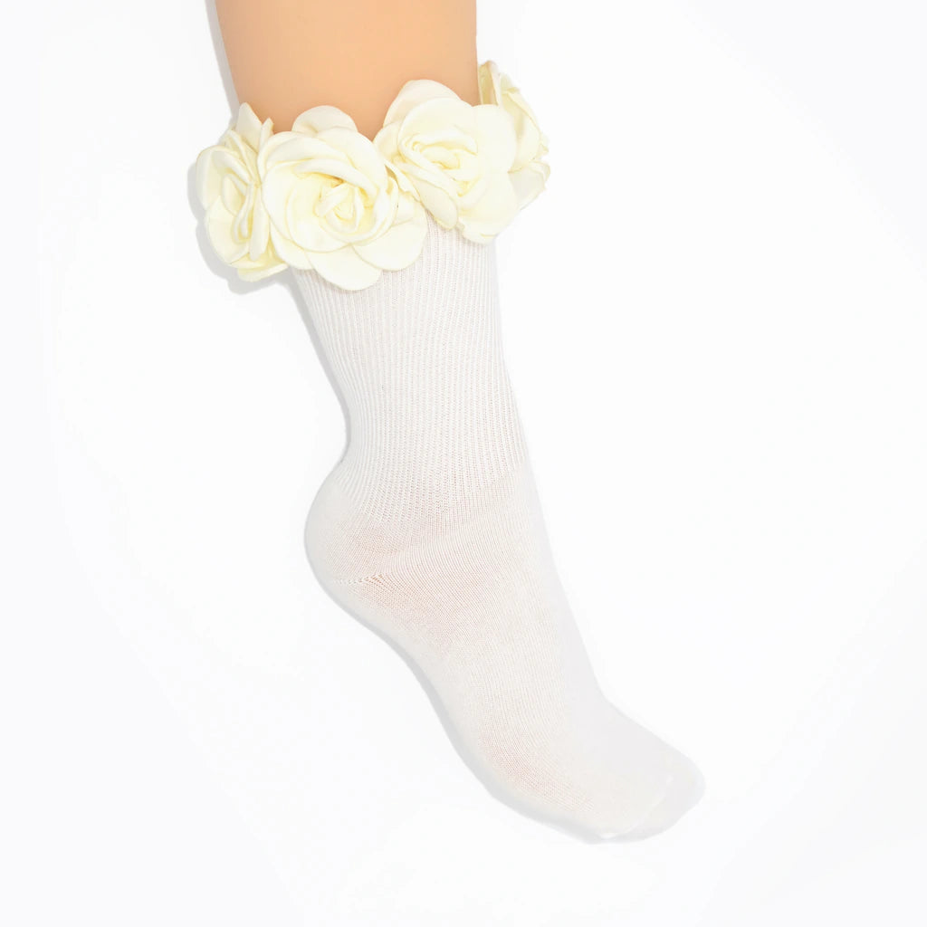 A white ribbed ankle sock with a large cream-colored fabric flower ruffle at the top, shown on a leg against a plain white background.
