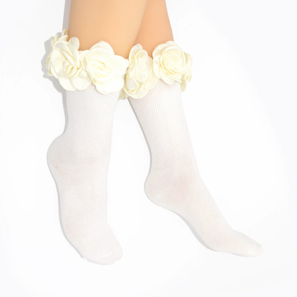 White ribbed crew socks with large white fabric roses around the top, shown on a person's legs against a plain white background.