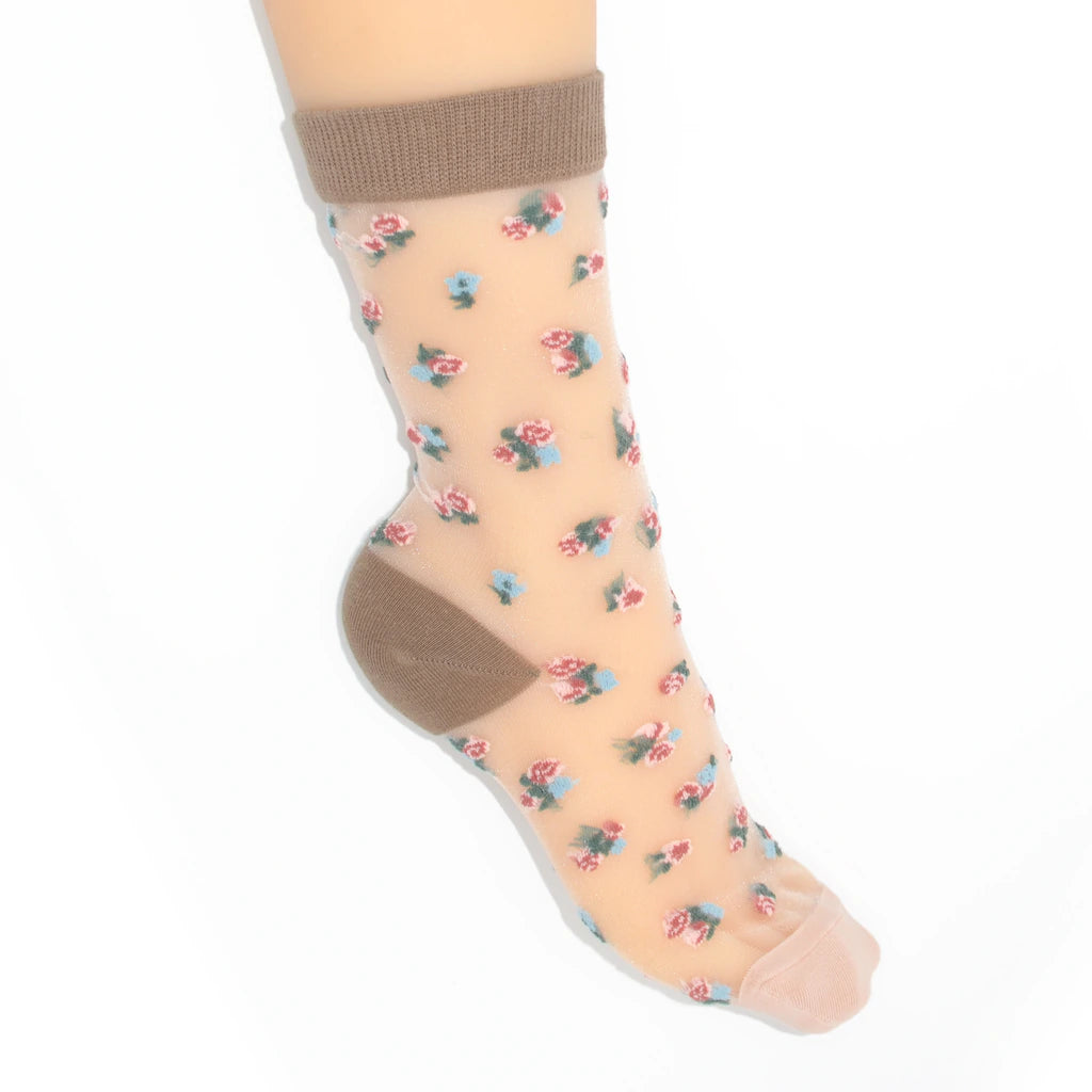A single ankle sock shown on a  foot against a plain white background. The sock is sheer nude beige with a small scattered floral print in pink, blue, and green, plus solid brown heel and toe sections.